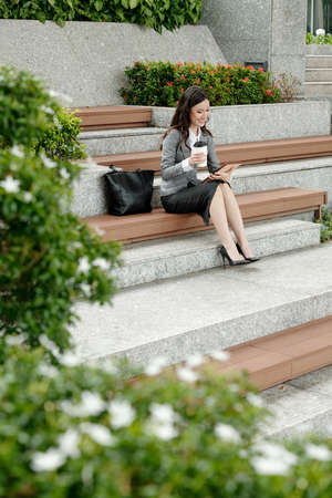 Female entrepreneur sitting on steps, drinking coffee and reading news article on tablet computerの写真素材