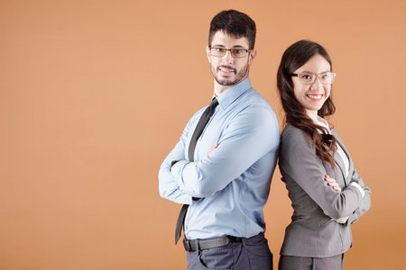 Confident smiling young businessman and businesswoman standing back to back, crossing arms and...