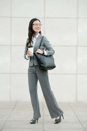 Portrait of elegant smiling businesswoman going to work with morning coffee in disposable cupの写真素材