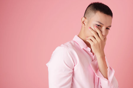 Portrait of sad pensive young man with makeup covering mouth and looking down