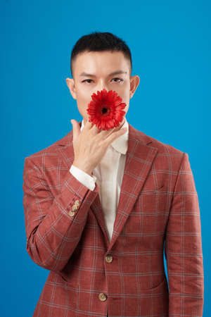 Portrait of young man in plaid suit jacket putting red blooming flower in mouthの写真素材