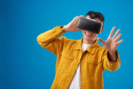 Positive young man testing new application for virtual reality headset, isolated on blue