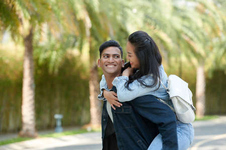 Portrait of smiling young man carrying his cheerful girlfriend when they are spending time in parkの写真素材