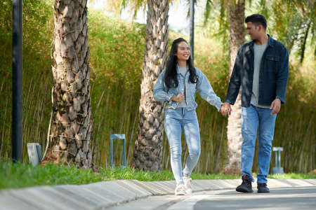 Happy young man and woman holding hands and walking in park on second dateの写真素材
