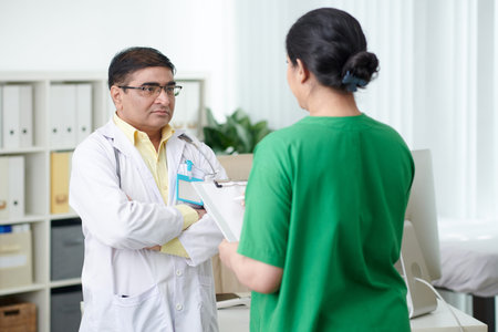 Serious general practitioner listening to medical nurse talking about problem of overflowing...