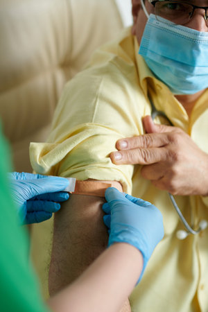 Hands of nurse sticking adhesive bandage on shoulder of patient after he got vaccine against new...