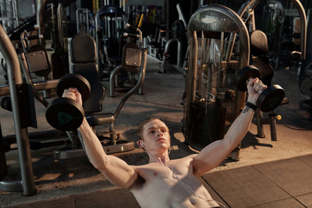 Strong shirtless young man doing bench press exercise in gym to tone muscles of the upper body