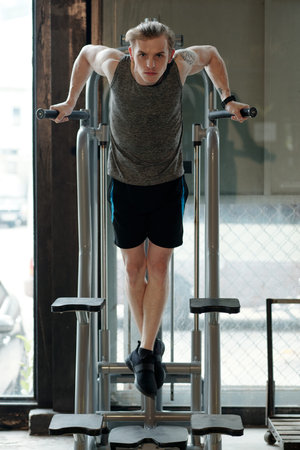 Fit young man doing exercise on pull-up machine when working out of triceps