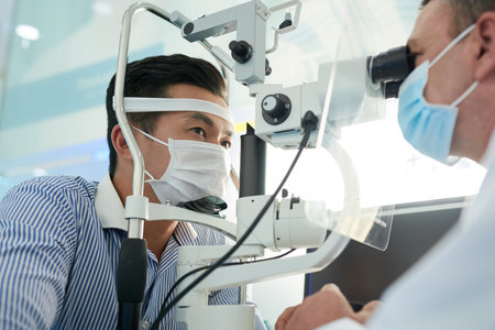 Doctor measuring intraocular pressure of patient in medical mask with special tool