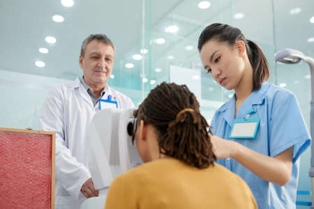 Nurse helping patient to put head in autorefractor so the doctor could measure the refractive error of the eyes and prescribe lensesの写真素材