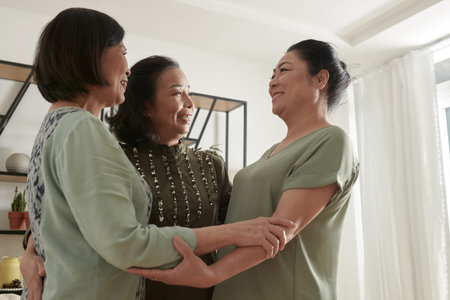 Cheerful senior friends hugging when having small party at home after not seeing each other for a...