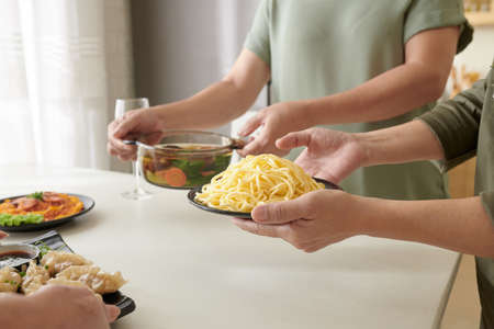 Senior women putting plates with delicious homemade food on dinner tableの写真素材