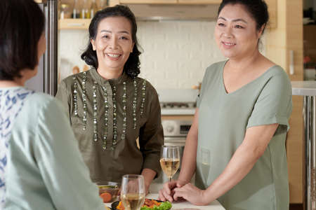 Smiling senior female friends gathered at home to chat over a glass of wineの写真素材