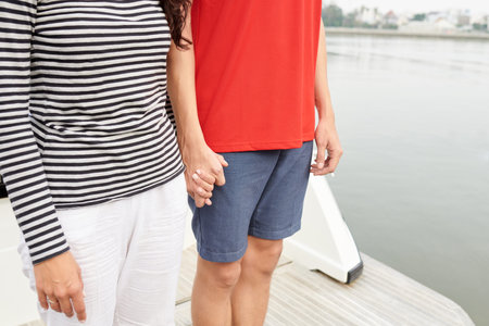 Young couple in comfy clothes standing on yacht and holding hands, sailing getaway concept