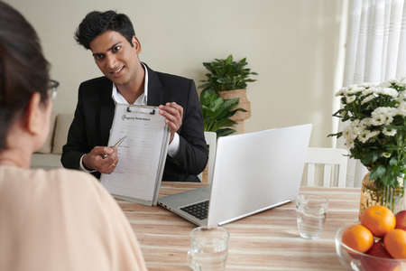Smiling insurance agent showing form to senior woman and explaining how to fill it to get property insuranceの写真素材