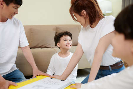 Cheerful little boy helping parents with packing suitcase for vacationの写真素材