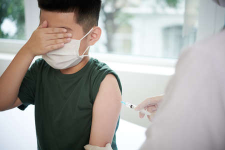 Little boy in mask closing his eyes with hands while doctor giving an injection from covid at hospitalの写真素材
