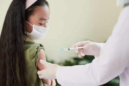 Close-up of nurse in protective gloves giving the Covid-19 vaccine to a girl due to coronavirus epidemicの写真素材