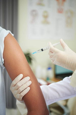 Doctor in mask giving an injection of a vaccine to a teenager girl in a medical clinic, vaccine...