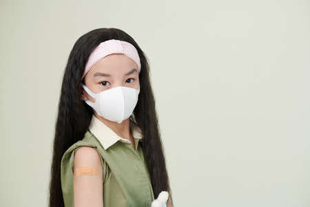 Portrait of ASian little girl in protective mask looking at camera against the white backgroundの写真素材