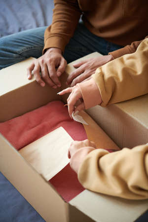 Close-up of young couple unpacking the cardboard box with new clothes together, they getting online orderの写真素材