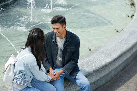 Smiling young man holding hands of girlfriend when telling how much he loves herの写真素材