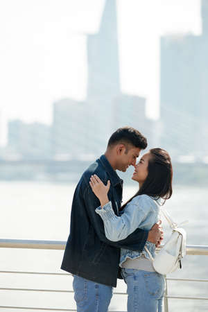 Beautiful young couple looking at each other and almost kissing when standing on bridgeの写真素材