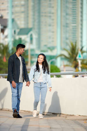 Smiling young couple in love holding hands when walking outdoors on sunny dayの写真素材