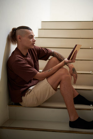 Young man in leisure wear sitting on steps with table computer and video calling colleague or friend...