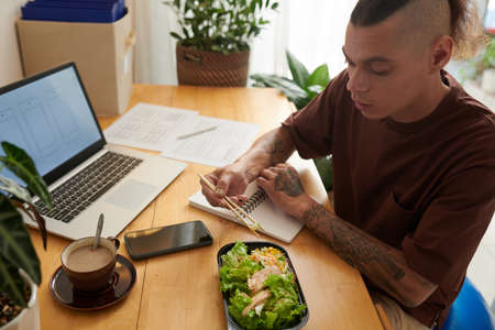 UI designer eating salad for lunch when thinking on new project at his home officeの写真素材