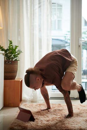 Strong young man watching tutorial on tablet computer when learning how to do handstandの写真素材