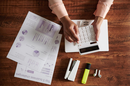 Hands of female entrepreneur checking statistics in business documents and making calculations