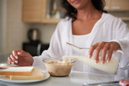 Woman pouring nondairy milk in bowl with granola when making breakfastの写真素材