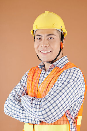 Studio portrait of smiling confident civil engineer in hardhat crossing arms and looking at camera
