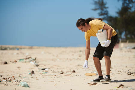 Young man picking garbage on sandy beach. Environmental pollution conceptの写真素材