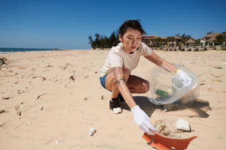 Young woman cleaning coastal zone and putting spilled garbage in big plastic bagの写真素材