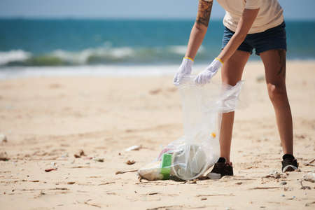 Cropped image of female volunteer picking up trash, plastic and glass bottles when cleaning up beach. Earth Dayの写真素材