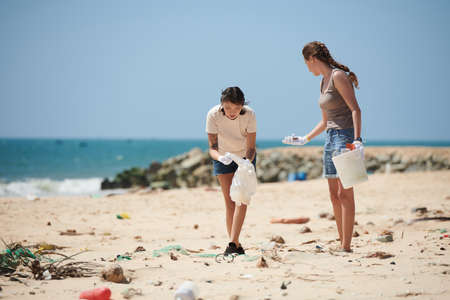 Female volunteers collecting plastic rubbish into bags on lake beach clean up dayの写真素材
