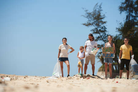 Group of activists standing on dirty beach with save the future poster after beach cleanup,on Earth dayの写真素材