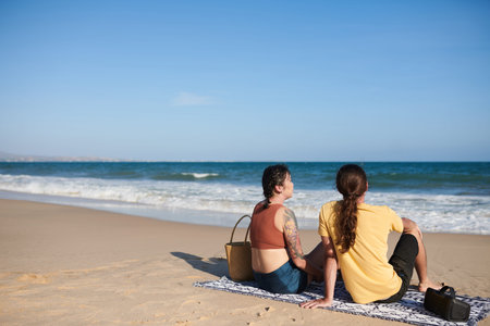 Young couple relaxing on beach, sitting on blanket and enjoying sea viewの写真素材
