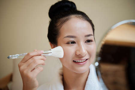 Smiling young woman applying liquid foundation with synthetic make-up brushの写真素材