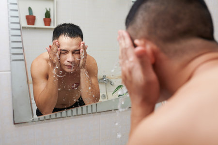 Asian young man washing face in bathroom, morning routine conceptの写真素材