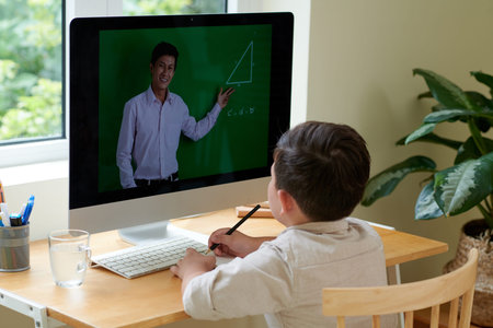 Schoolboy watching geometry lesson on computer and drawing in textbook