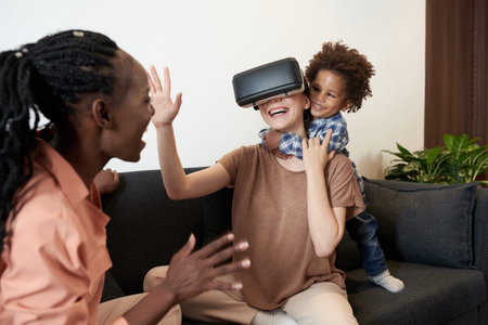 Excited toddler boy hugging mother in virtual reality headset playing video game