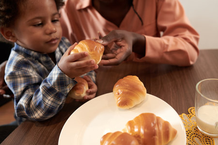 Mother giving freshly baked croissants to little son for breakfastの写真素材