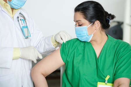 Medical nurse getting second shot of vaccine against coronavirus in hospitalの写真素材