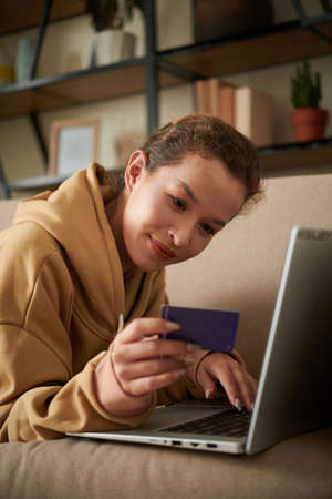 Cheerful young woman entering information from credit card when paying for online purchaseの写真素材