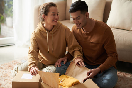 Joyfu young couple opening boxes with clothes they ordered for each other