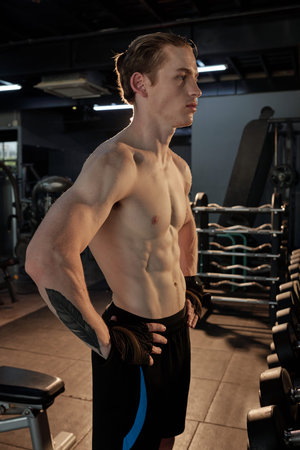 Seriuous fit young man with perfect abs muscles resting between exercise sets in gym