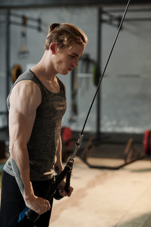 Determined strong young man doing cable pull down exercise to sculpt and build tricep muscles